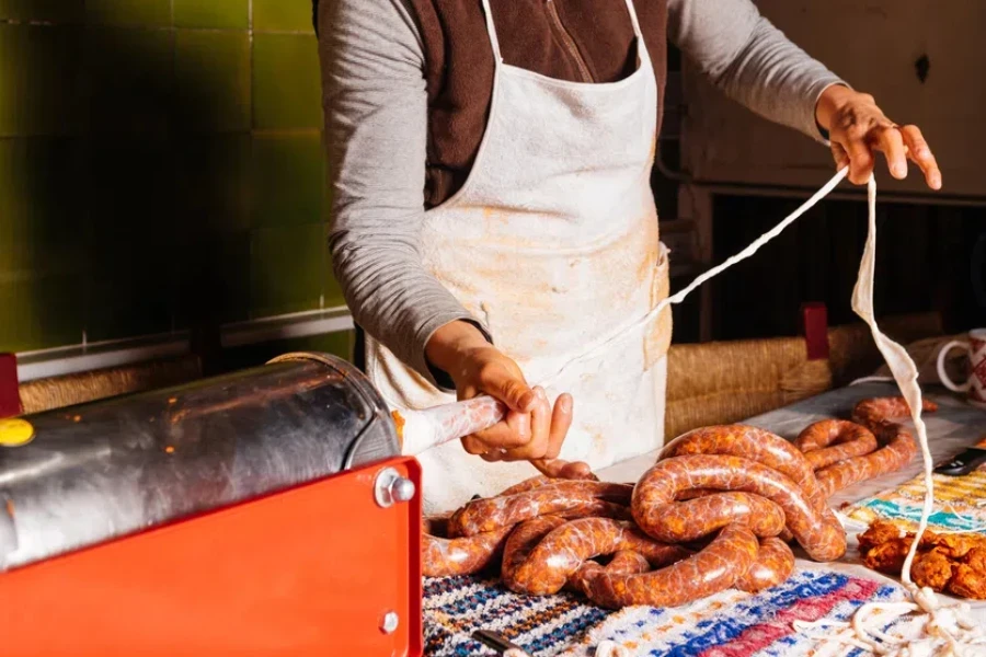 Woman using horizontal stuffer machine to prepare homemade chorizo sausages in kitchen