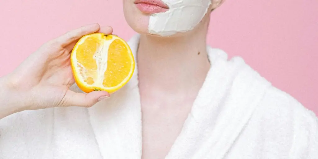 Woman with face mask holding orange halves against a pink background