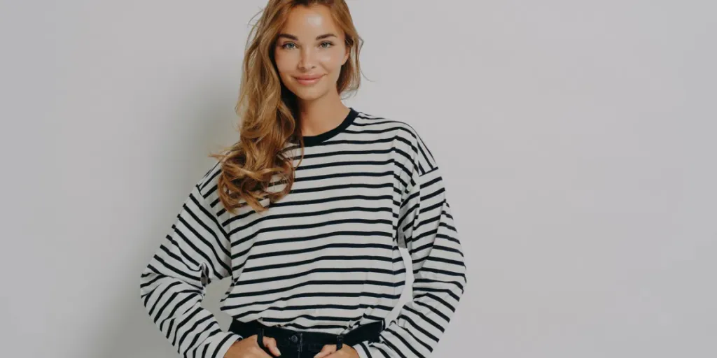 Young confident charming woman in striped blouse and casual jeans standing with hands on waist