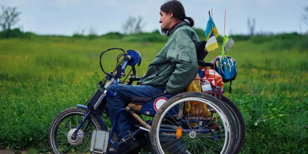 Un jeune homme handicapé en fauteuil roulant conduit le long de la route dans le champ