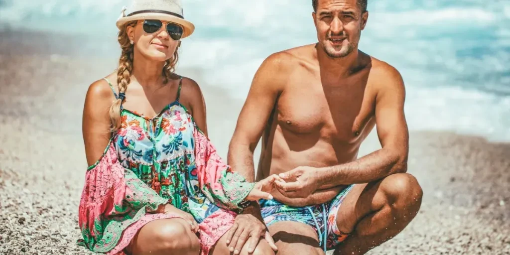 Young man and woman are posing on the sea beach in summer day and looking at camera