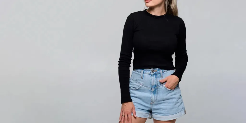 Young slim woman in a black basic long sleeve sweater and jorts on light background