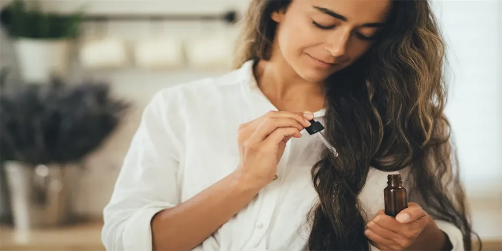 Mujer joven aplicando aceite esencial orgánico natural en el cabello y la piel.