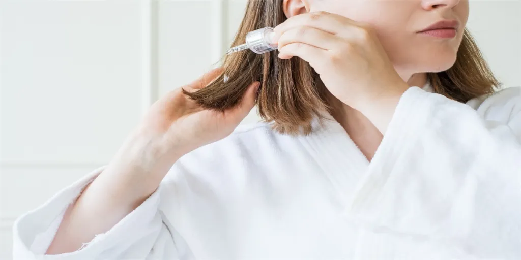 Mujer joven aplicándose aceite en el cabello con una pipeta sobre fondo blanco