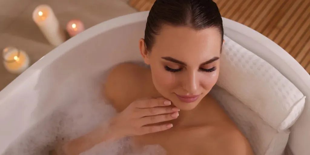 Young woman using pillow while enjoying bubble bath indoors1