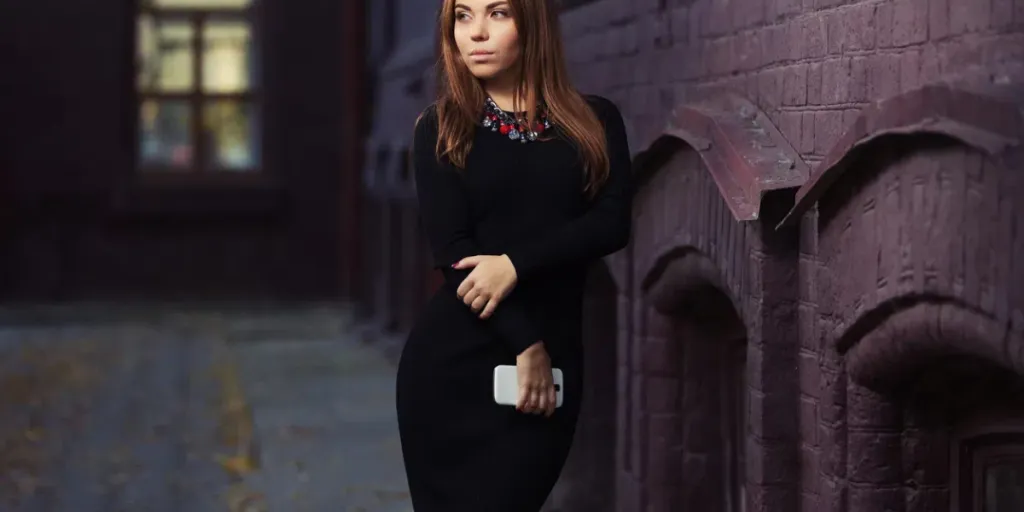 Young woman with a cell phone walking on city street Stylish fashion model with long straight hair in black sweater dress