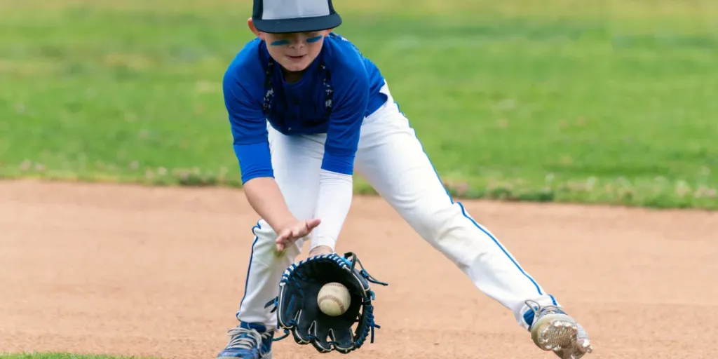 Youth baseball player in blue uniform fielding a ground ball into his glove in the infield during a game