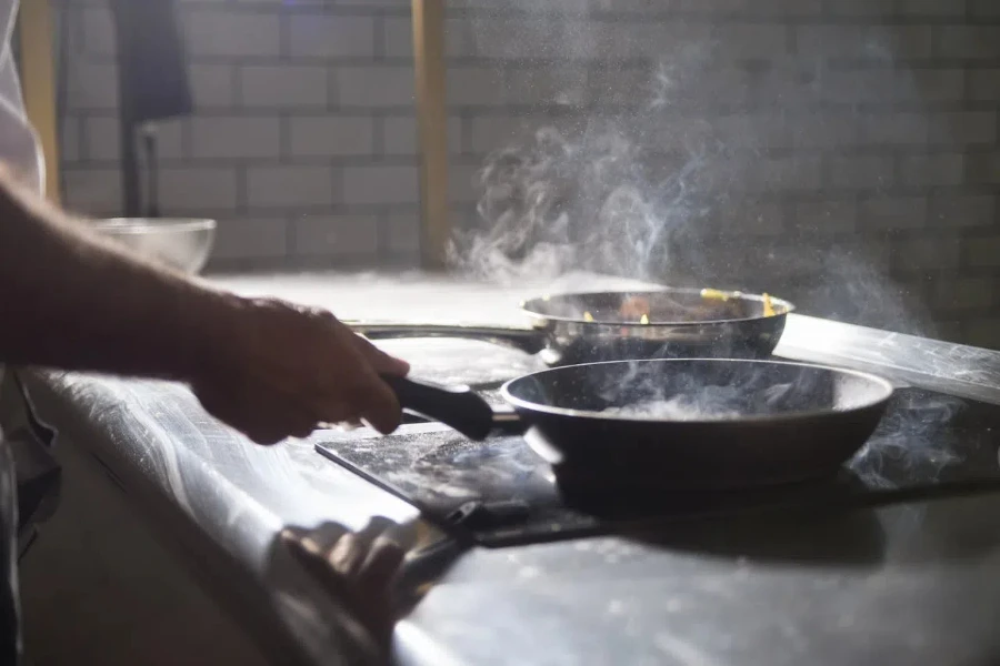 Una mano che tiene una padella calda mentre cucina su un fornello elettrico