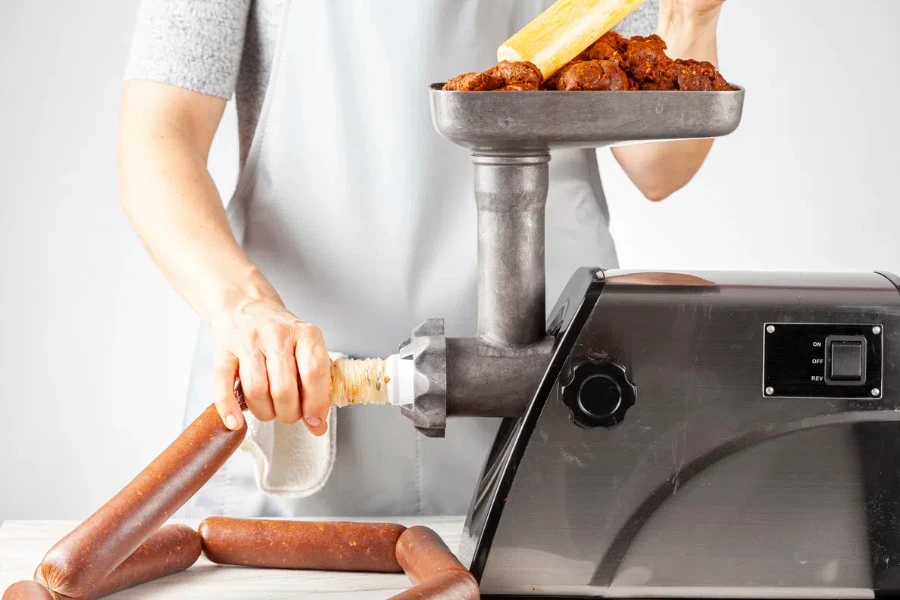 a woman cook wearing apron is stuffing homemade sucuk or sausage into casing