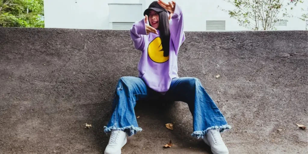 Hermosa adolescente con sudadera y gorra sentada en la ciudad en estilo urbano posando para la cámara