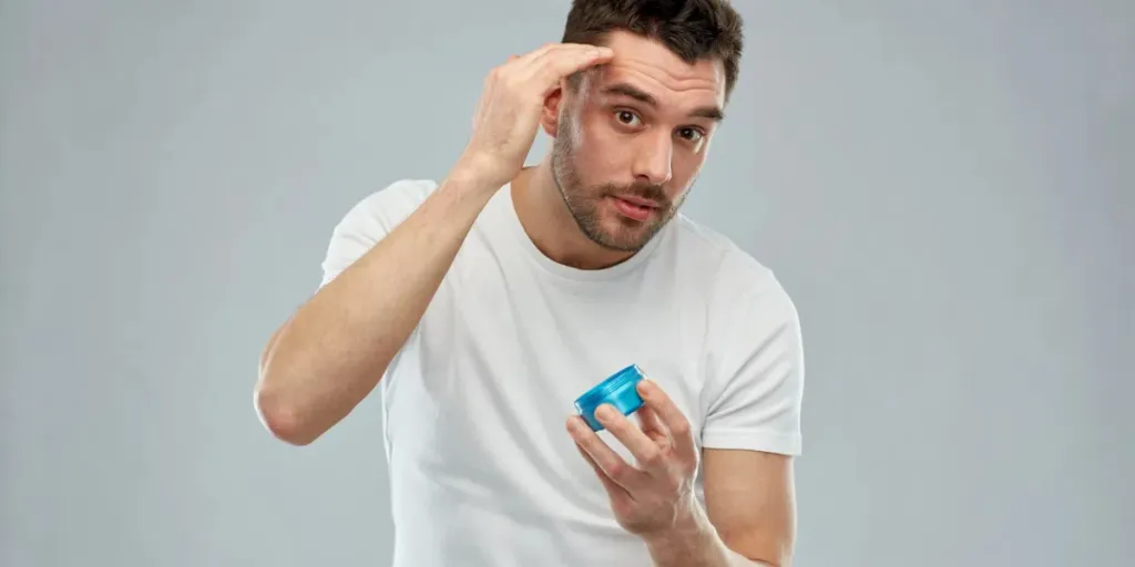 Joven feliz peinándose el cabello con cera o gel sobre fondo gris