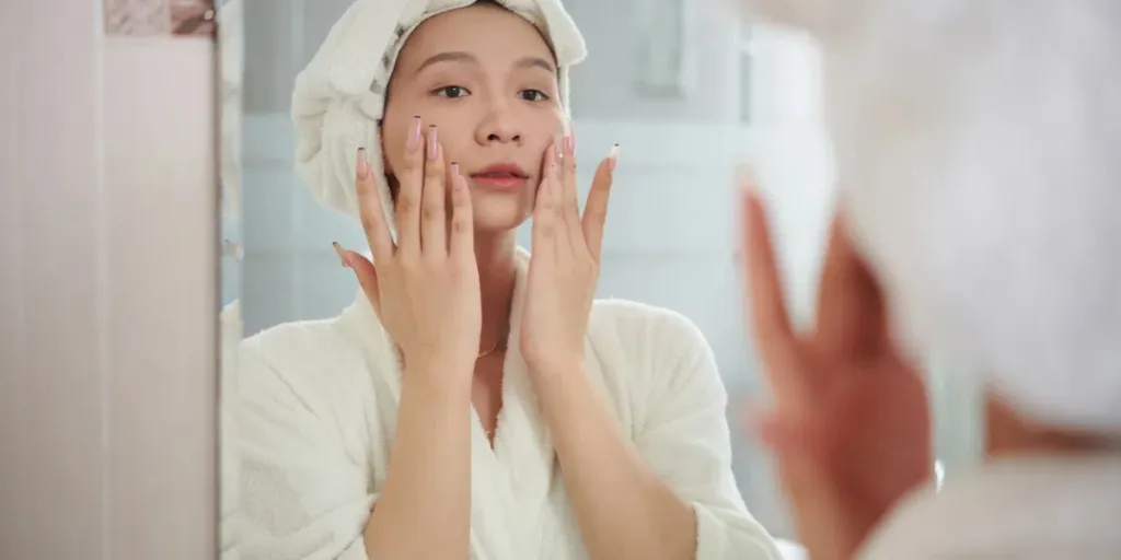 woman in bathrobe applying moisturizing lotion