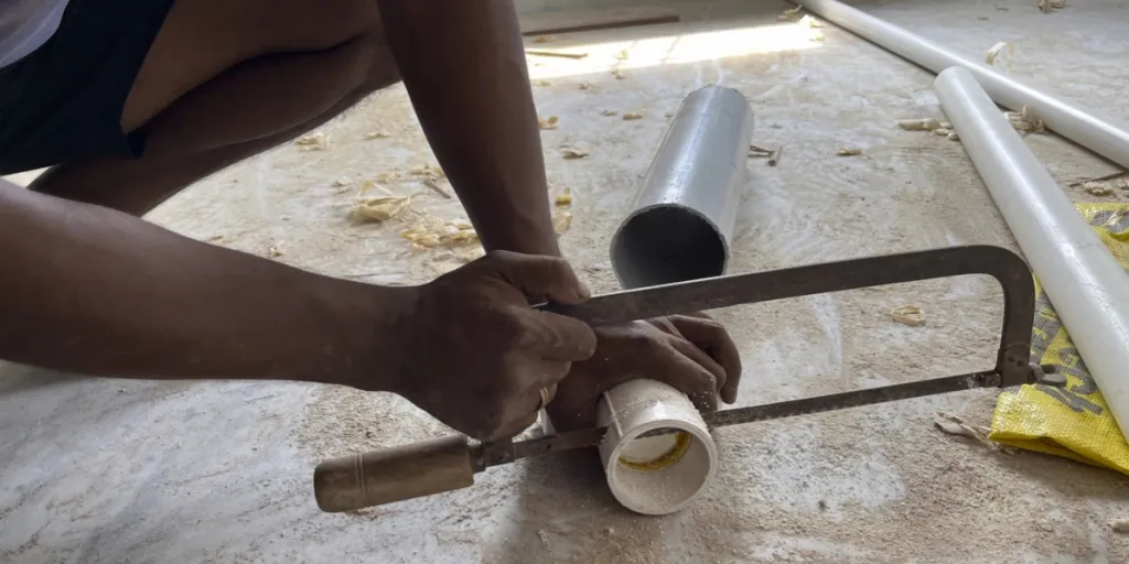 Un homme coupe un tuyau avec une lame de scie