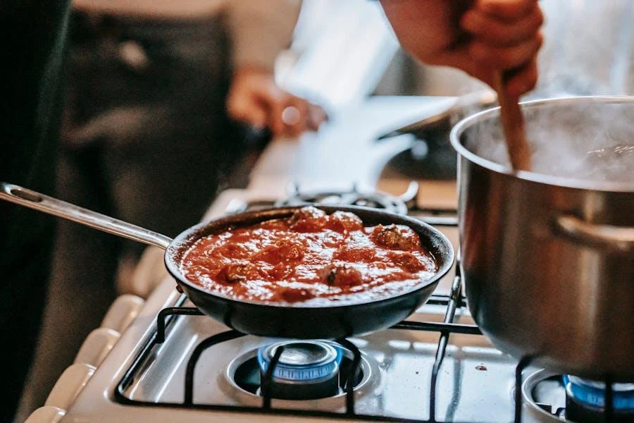 A person stirring a pot and a pan on top of a stove gas cooker