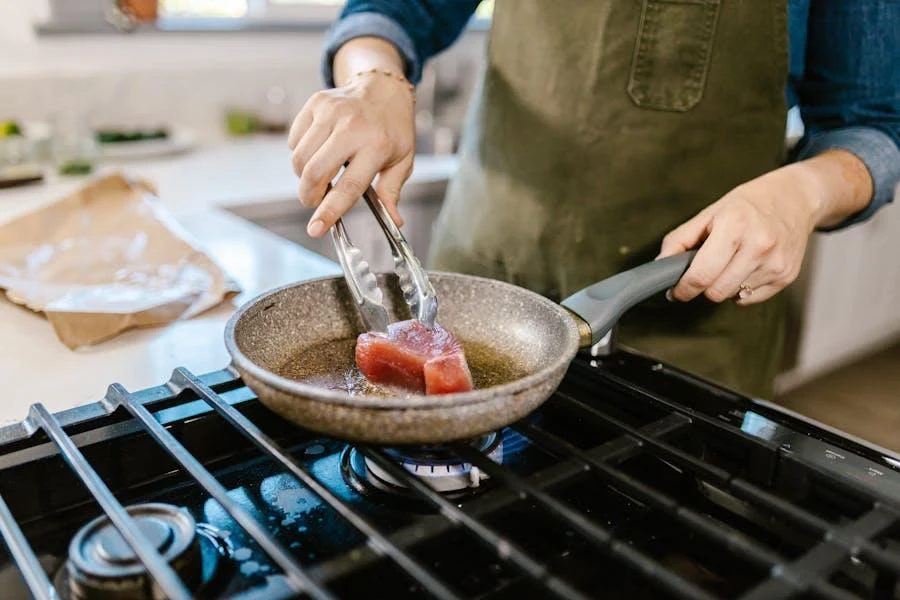 A person using a stove gas cooker to cook steak in a pan