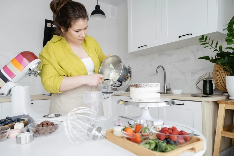 A woman decorates a cake in a modern kitchen, preparing icing with fresh ingredients