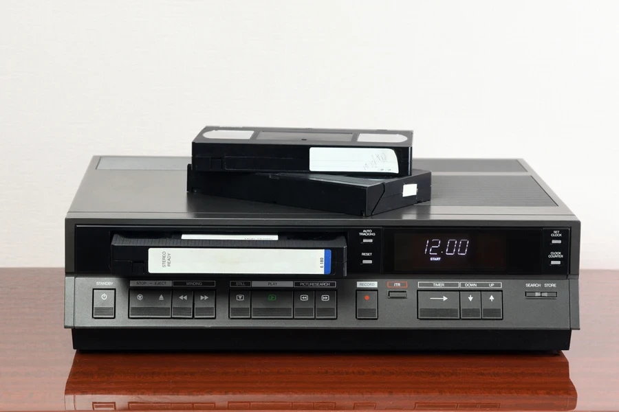 An old vintage videotape recorder from the 1980s stands on a dark table with a videotape