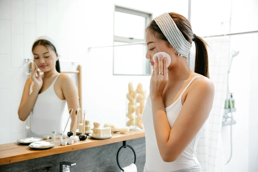 Asian woman applying skincare with cotton pad in bright bathroom setting