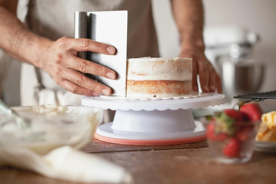 Close-up of a baker applying frosting on a fresh cake indoors