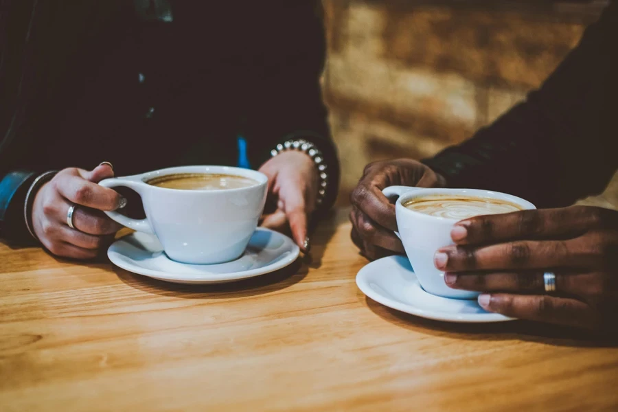 Close-up of two people holding cups of coffee at a café table, creating a cozy atmosphere