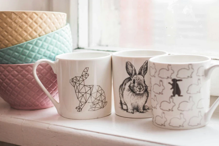 Elegant ceramic mugs with rabbit designs and colorful bowls on a windowsill