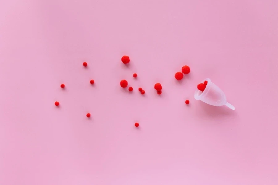 Copo menstrual com elementos vermelhos sobre fundo rosa simbolizando menstruação e feminilidade