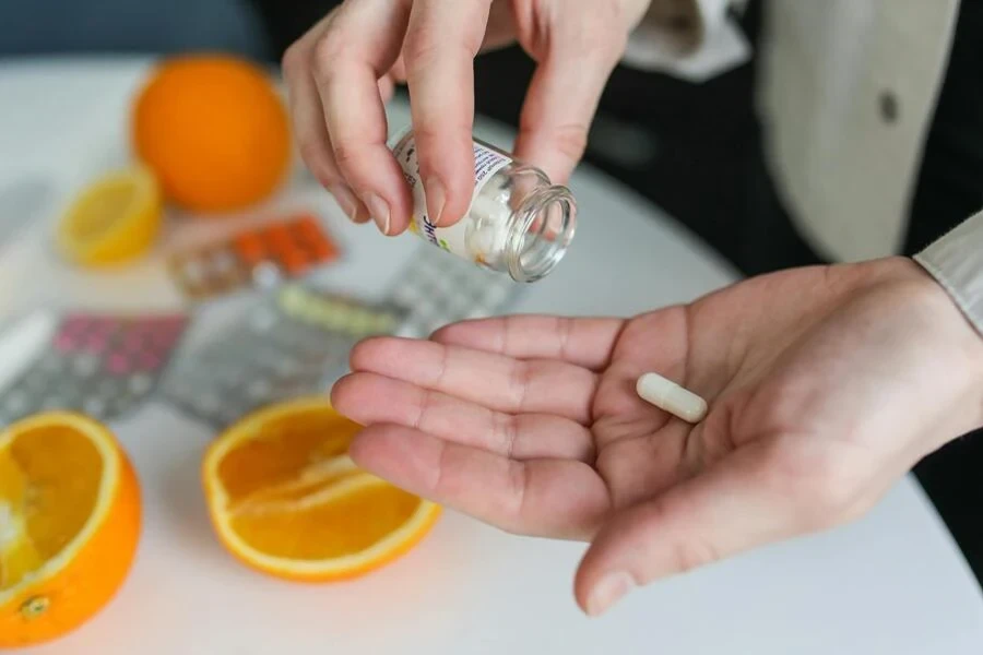 Person taking a pill from a glass bottle