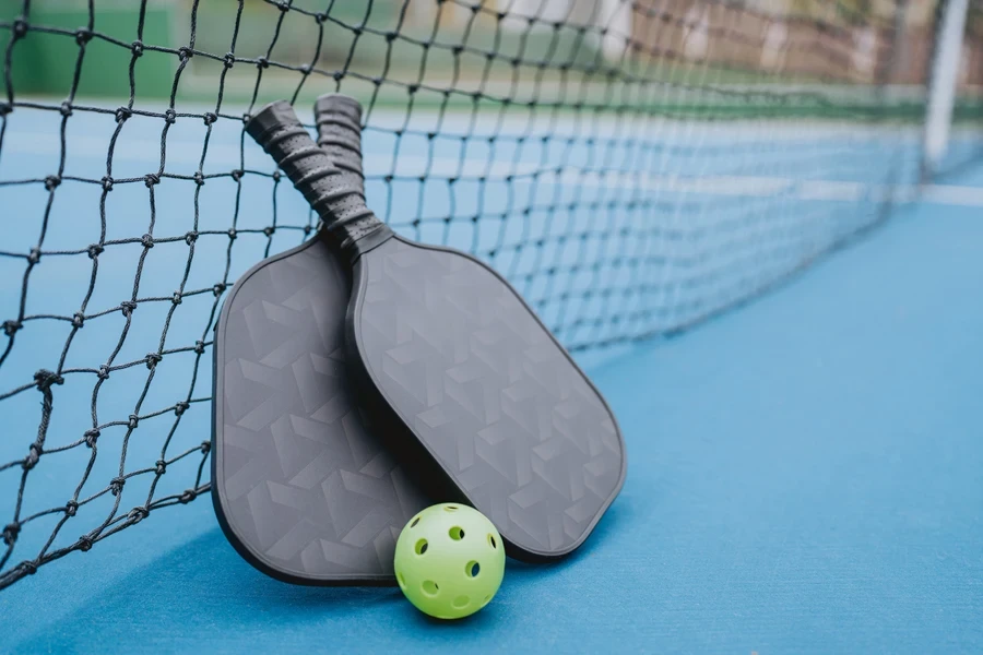 Two black pickleball paddles with yellow ball on court