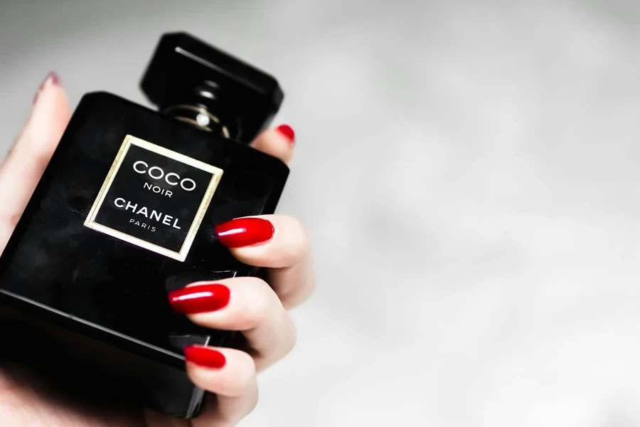 Femme aux ongles rouges tenant un parfum