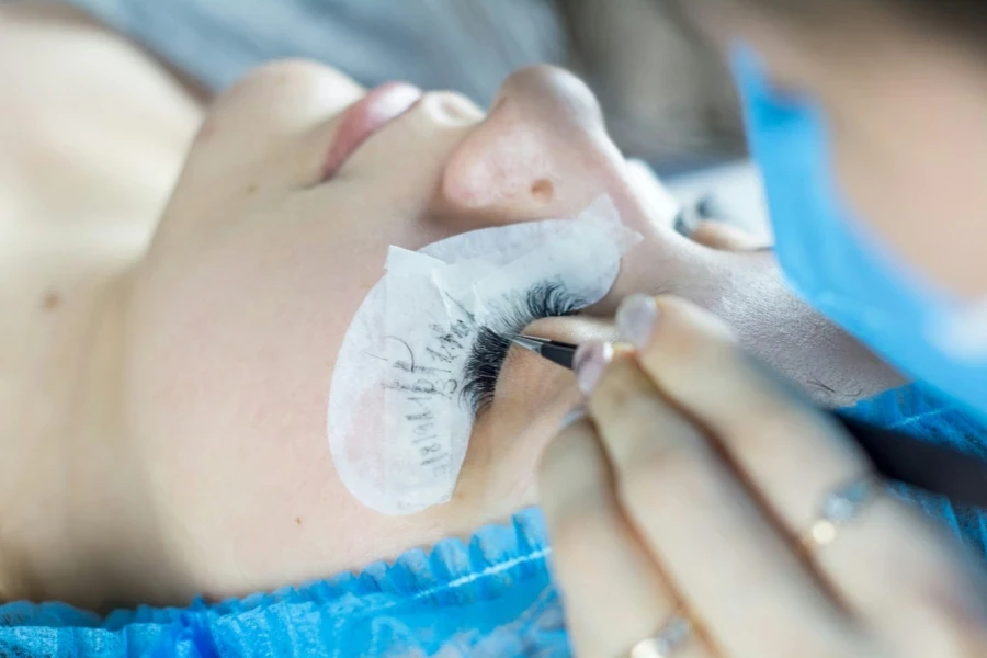 Young woman undergoing eyelash extensions procedure, closeup.