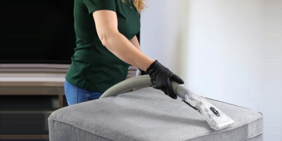 a woman in a green shirt and black gloves vacuuming a gray ottoman