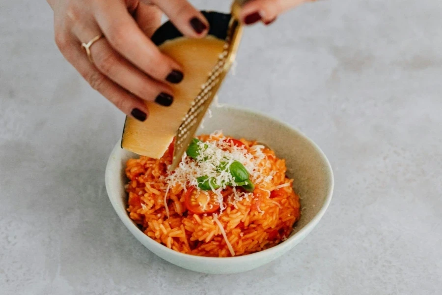 Eine Person reibt Käse auf Risotto in der Schüssel