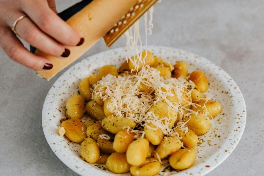 Eine Person reibt Käse auf einem Gnocchi