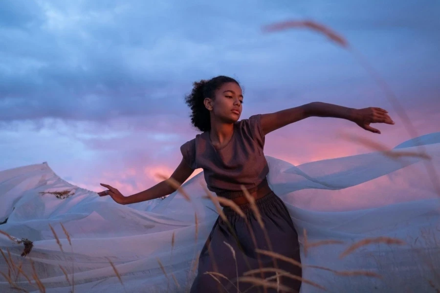 A Woman in a Brown Dress Dancing by a White Cloth