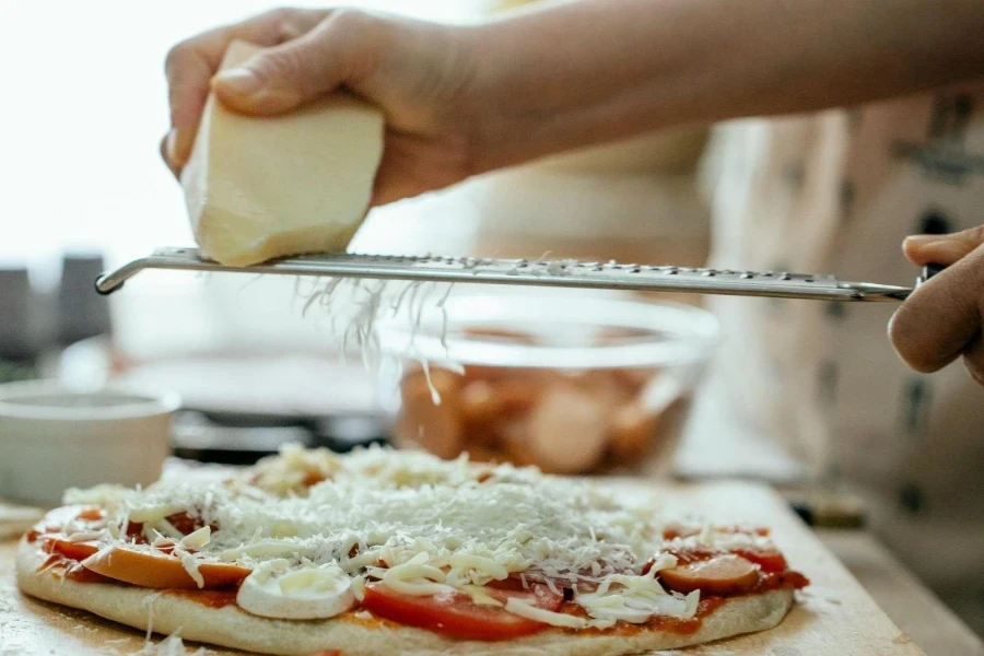 Anonyme Person reibt Käse auf Pizza