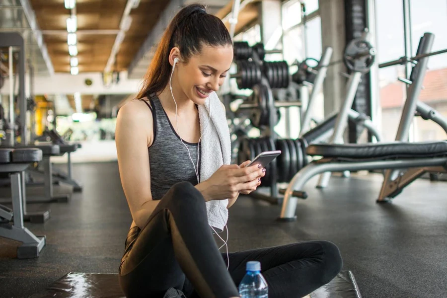 Mujer atractiva y en forma usando el teléfono después del entrenamiento deportivo en el gimnasio