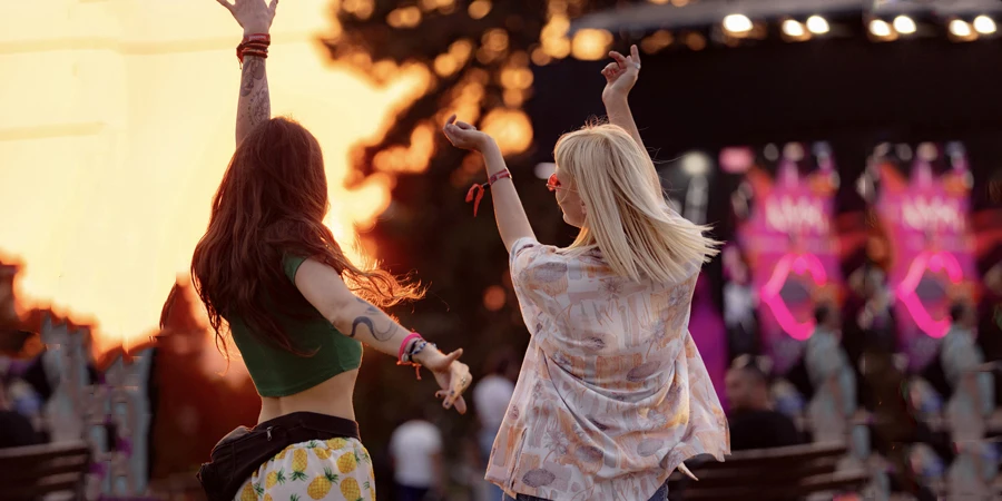 Wanita-wanita riang bersenang-senang sambil menari di festival musik luar ruangan saat matahari terbenam.