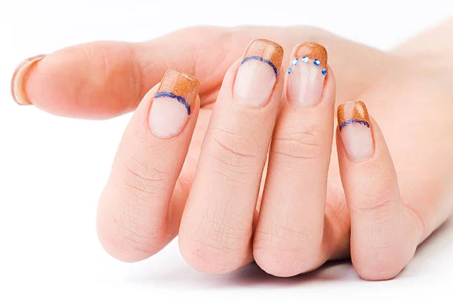 French tip nails painted with orange glitter and blue detailing