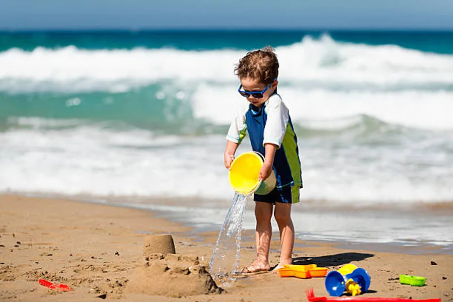 Little Boy Pouring Water on Sand Castle