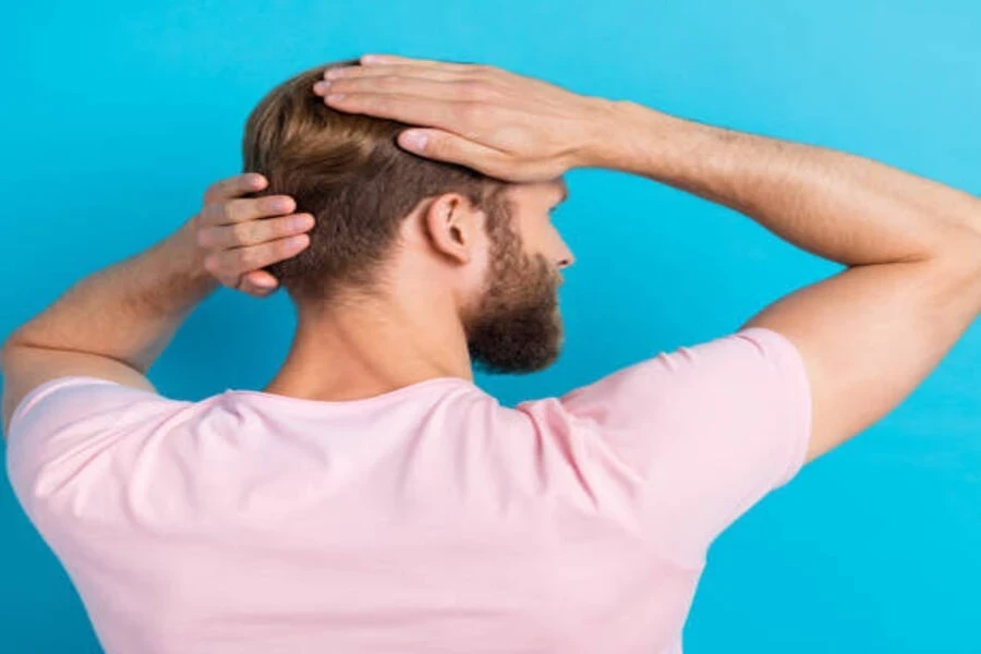 Un homme portant un t-shirt rose touchant ses cheveux lissés en arrière