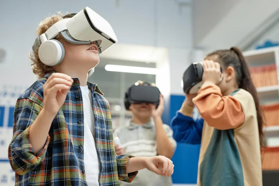 Portrait of excited blonde boy wearing VR headset in school library and enjoying 360 learning experience copy space