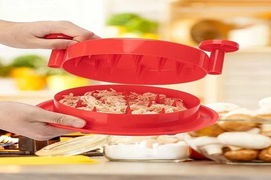 Red plastic manual chicken shredder with meat inside