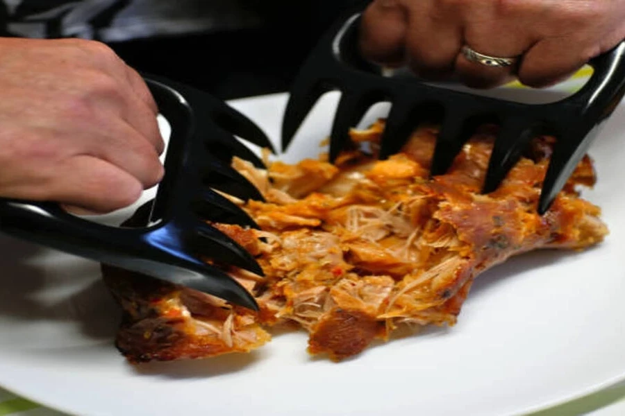 Dos garras de plástico negro para desmenuzar carne utilizadas con pollo.