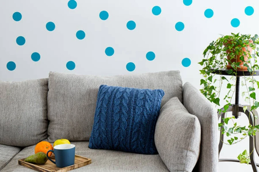 Konsep hiasan dinding. Dinding ruang tamu dihiasi dengan pelekat dinding corak polka dot biru. Sofa dengan dulang dan tanaman rumah pasu.