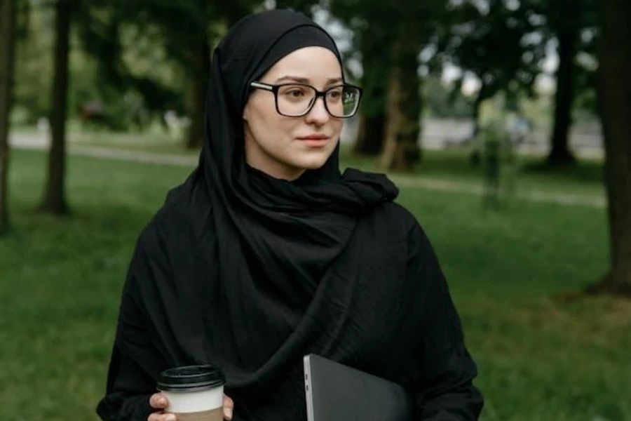 Donna che indossa l'hijab Chador e tiene in mano un caffè e un computer portatile