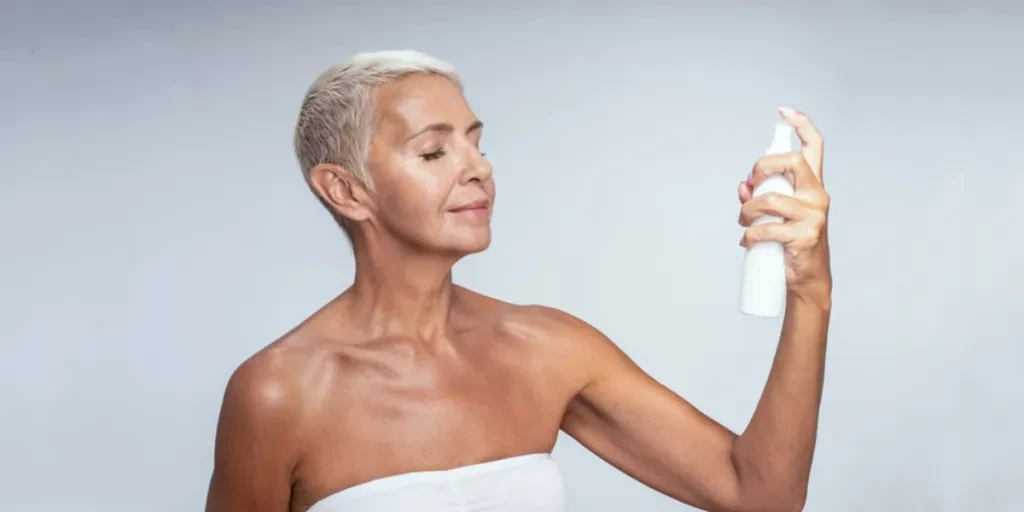 Donna che tiene in mano una bottiglia spray e si spruzza il viso