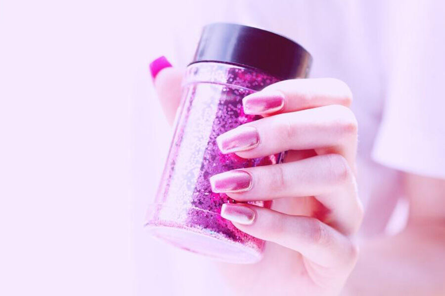 рука с радужными розовыми ногтями, держащая розовый крупный блеск