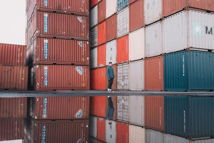 Hombre en top verde y pantalones de pie junto a contenedores de envío