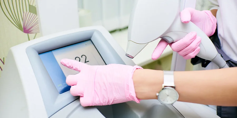 Hands of the doctor in pink gloves hold the device for an epilation and press the touch screen. The concept of control device, laser hair removal