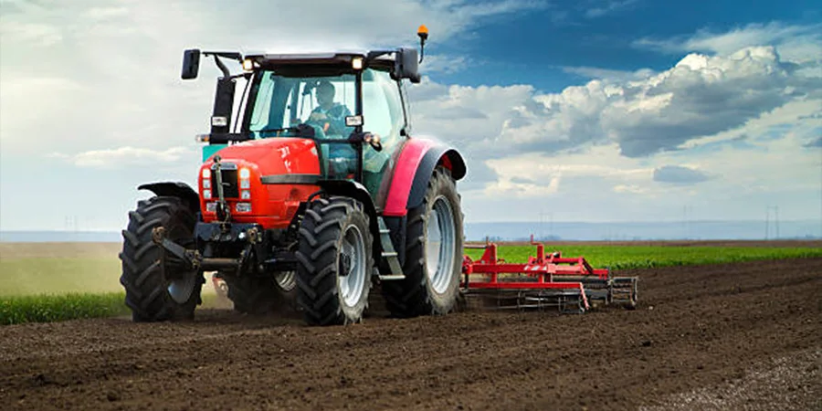 A red agriculture tractor cultivating a field